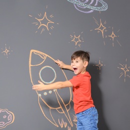 Photo of Cute little child playing with chalk rocket drawing on grey background