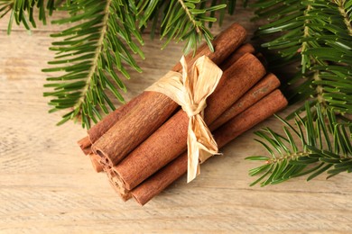 Photo of Bunch of cinnamon sticks and fir branches on wooden table, top view