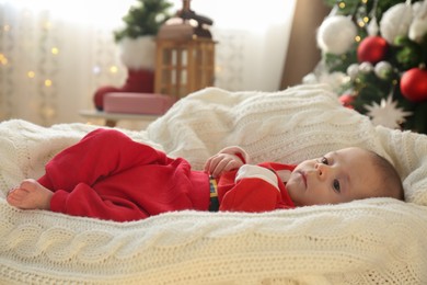 Cute little baby on knitted blanket in room decorated for Christmas