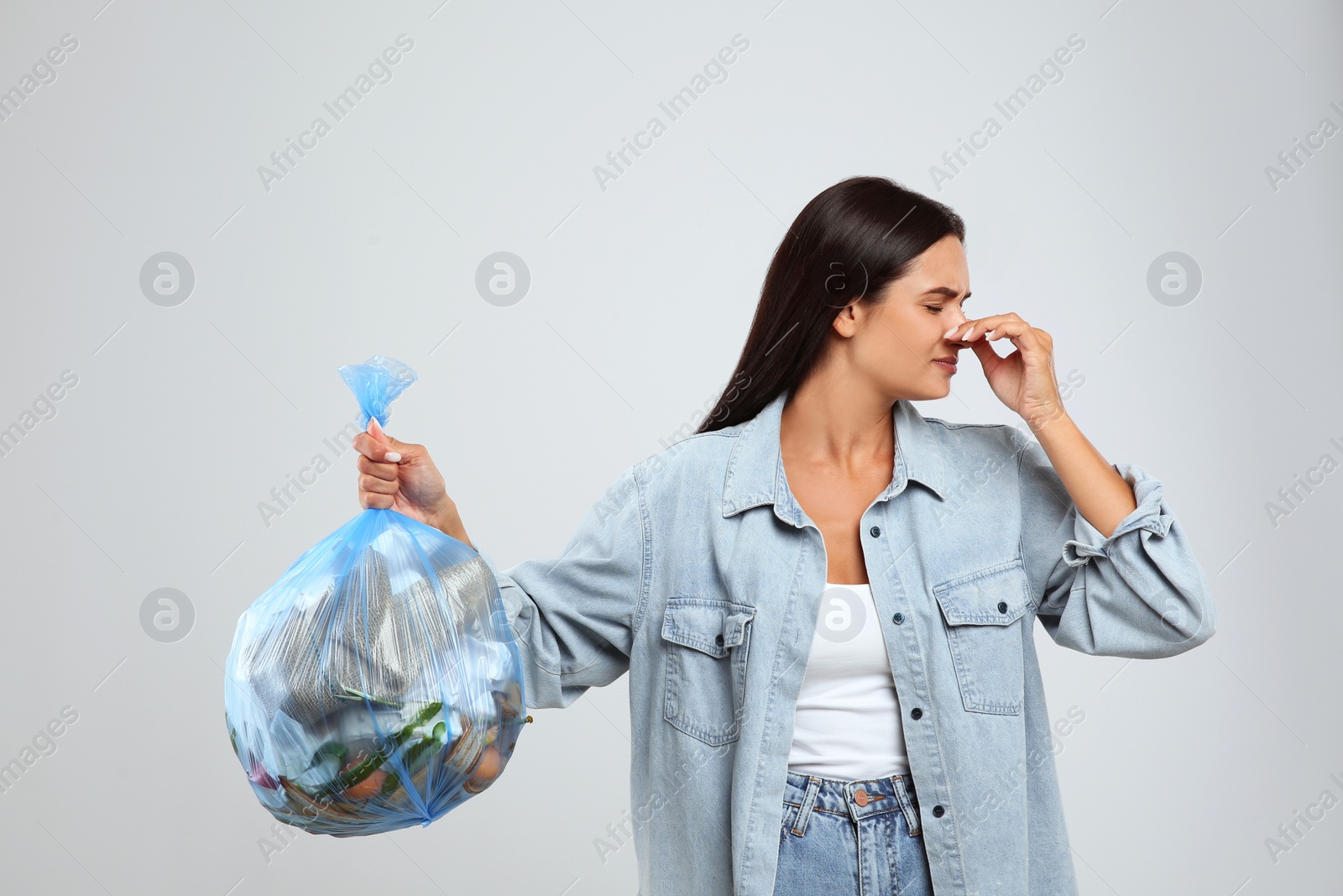 Photo of Woman holding full garbage bag on light background