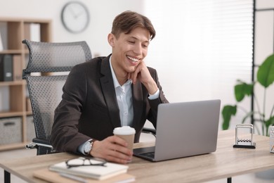 Man with cup of coffee watching webinar at wooden table in office