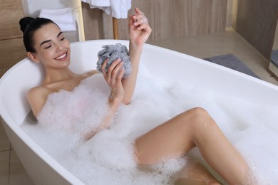 Photo of Woman taking bath with mesh pouf in bathroom