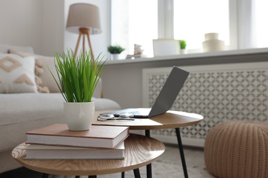 Photo of Potted artificial plant, laptop and books on wooden nesting tables indoors