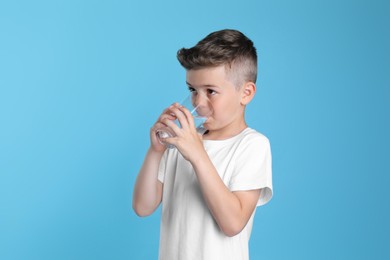 Cute little boy drinking water from glass on light blue background