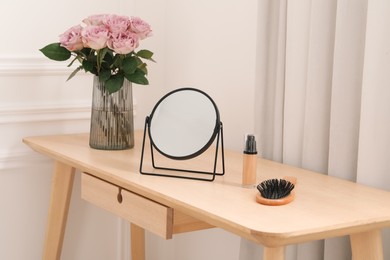 Photo of Mirror, foundation, brush and vase with pink roses on wooden dressing table in makeup room