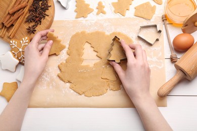 Photo of Woman making Christmas cookies with cutters at white wooden table, top view