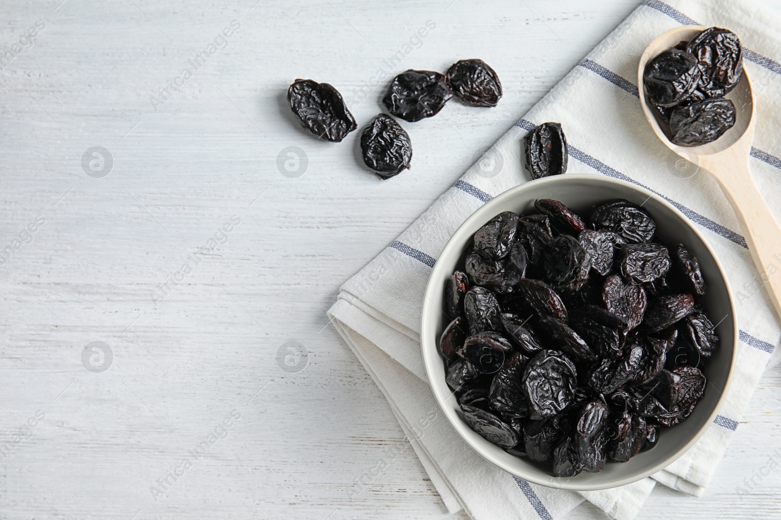 Photo of Bowl and spoon of sweet dried plums on table, top view with space for text. Healthy fruit