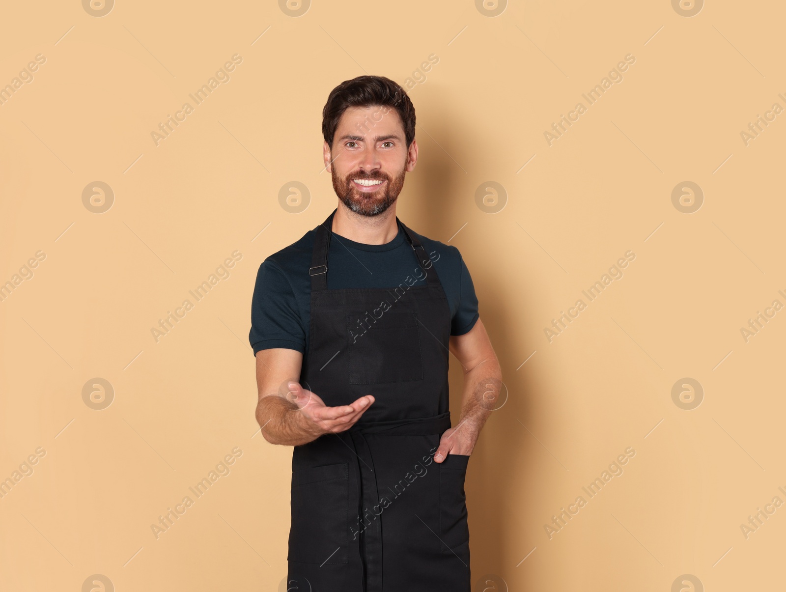 Photo of Smiling hairdresser wearing apron on light brown background