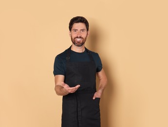 Photo of Smiling hairdresser wearing apron on light brown background