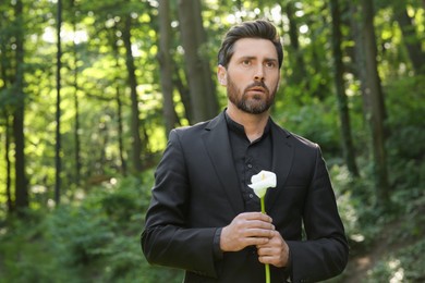 Photo of Sad man with calla lily flower outdoors. Funeral ceremony