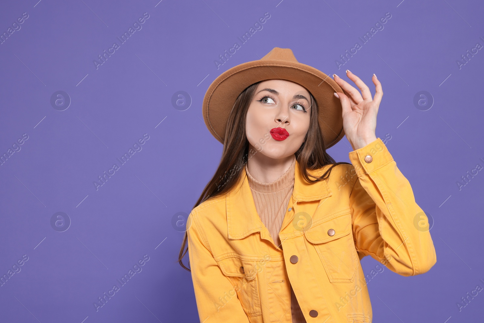 Photo of Beautiful young woman blowing kiss on purple background, space for text