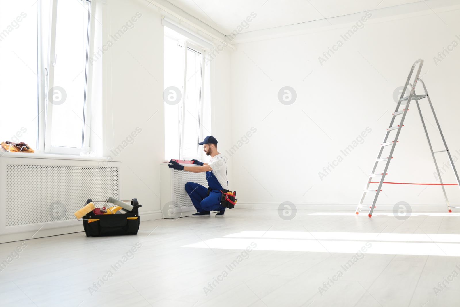 Photo of Handyman in uniform working with building level indoors, space for text. Professional construction tools