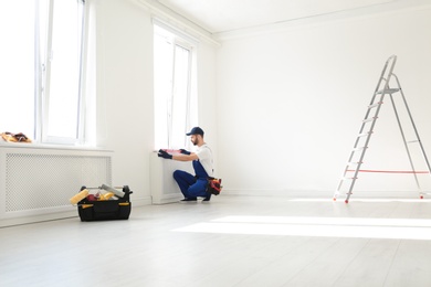 Handyman in uniform working with building level indoors, space for text. Professional construction tools