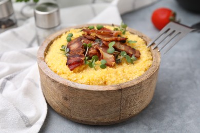 Photo of Cooked cornmeal with bacon and microgreens in bowl on light grey table, closeup