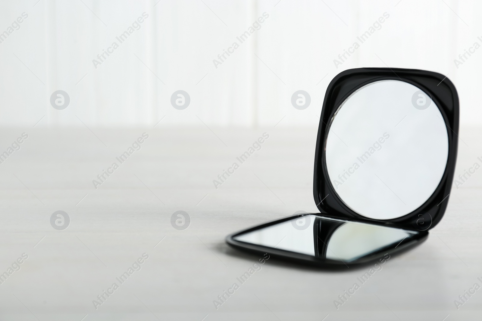 Photo of Stylish cosmetic pocket mirror on white wooden table. Space for text