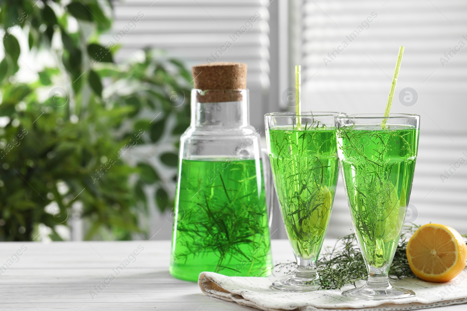 Photo of Homemade refreshing tarragon drink, sprigs and lemon on white wooden table, space for text