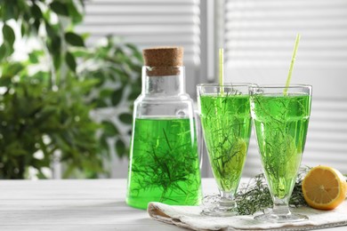 Photo of Homemade refreshing tarragon drink, sprigs and lemon on white wooden table, space for text