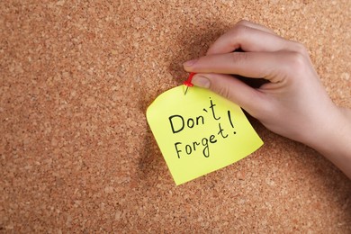 Woman pinning paper note with phrase Don't Forget to cork board, closeup