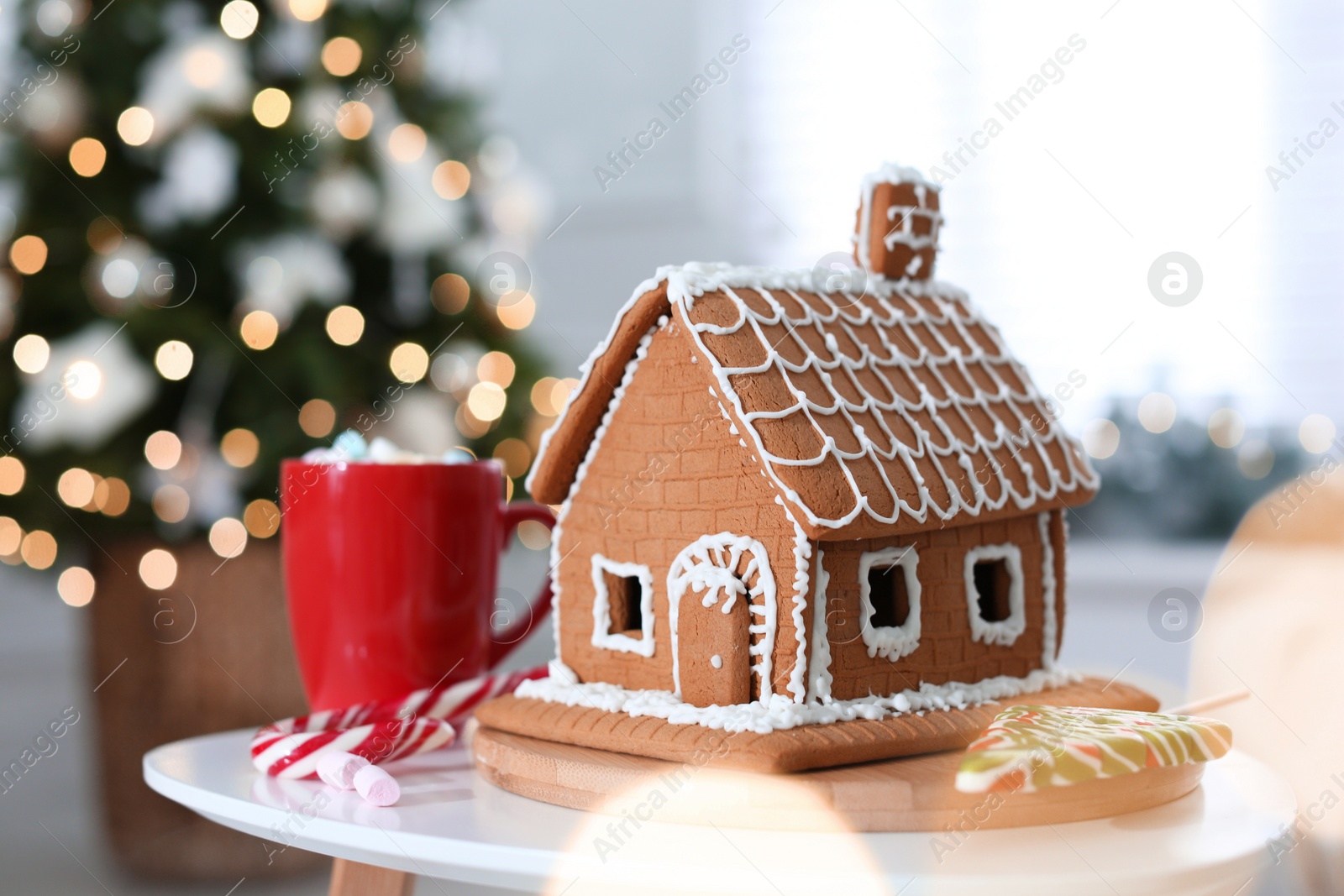 Photo of Beautiful gingerbread house decorated with icing on white table indoors