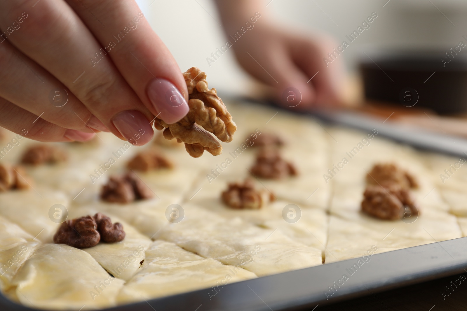 Photo of Making delicious baklava. Woman putting walnut onto dough, closeup