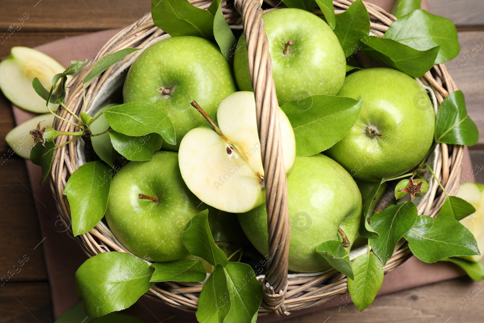 Photo of Fresh ripe green apples and leaves with wicker basket on wooden table, flat lay