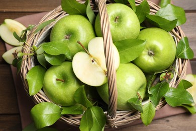 Photo of Fresh ripe green apples and leaves with wicker basket on wooden table, flat lay