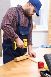 Photo of Young worker using electric drill at table in workshop