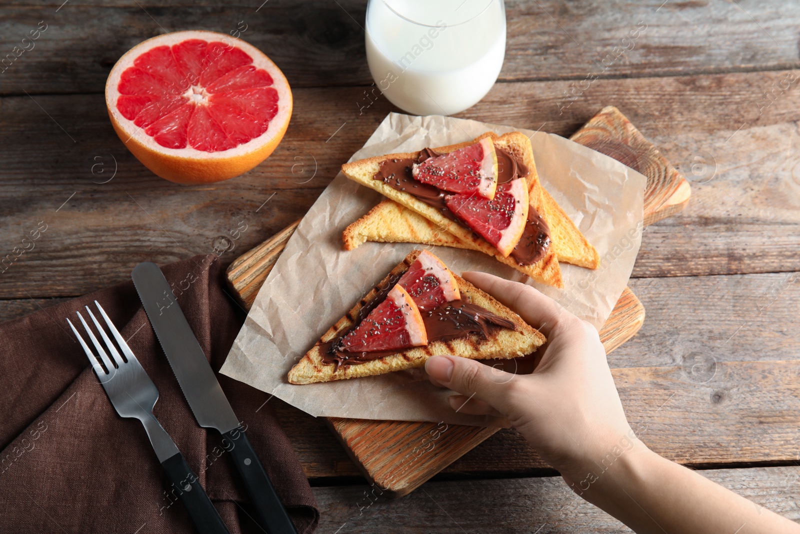 Photo of Woman eating toasts with grapefruit, chocolate paste and chia seeds at table, top view