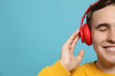 Handsome young man with headphones on light blue background, closeup. Space for text