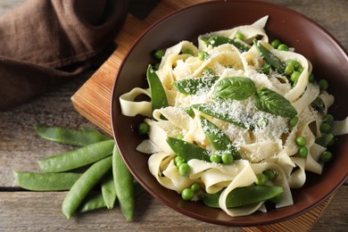 Photo of Delicious pasta with green peas, fresh basil and cheese on wooden table, above view