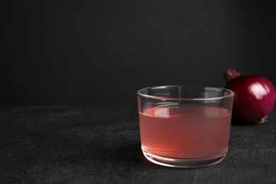 Photo of Glass of onion syrup and fresh vegetable on dark table. Space for text