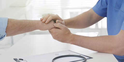 Doctor holding senior patient's hand in office, closeup. Banner design