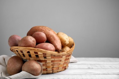 Photo of Different types of fresh potatoes in wicker basket on white wooden table, space for text
