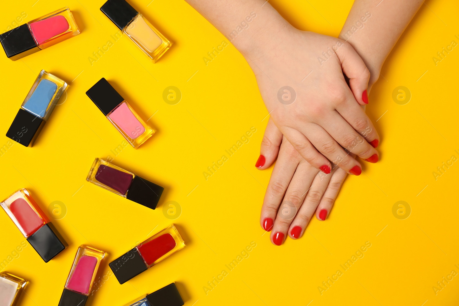 Photo of Woman with red manicure and nail polish bottles on color background, top view