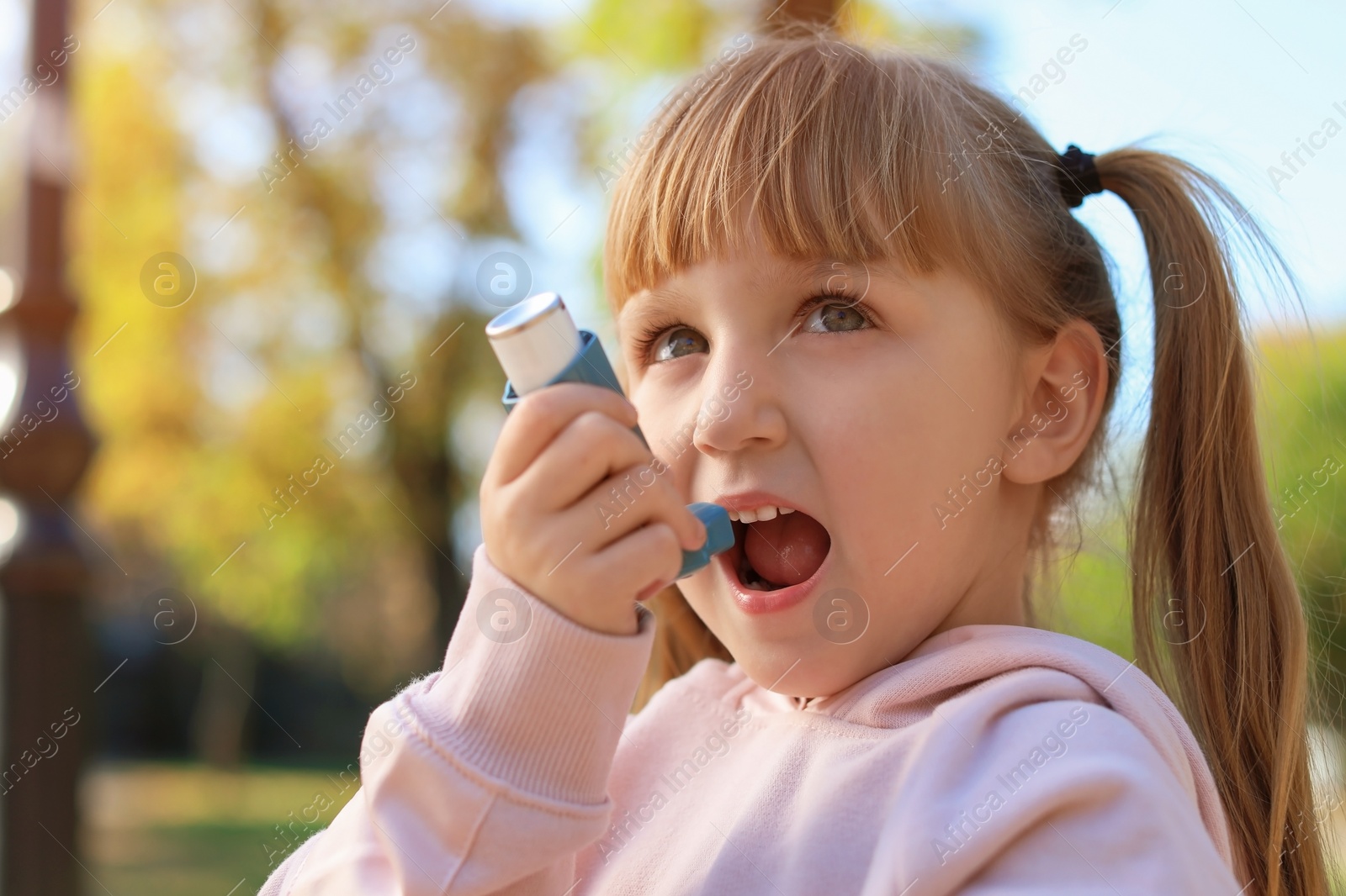 Photo of Little girl using asthma inhaler outdoors. Health care