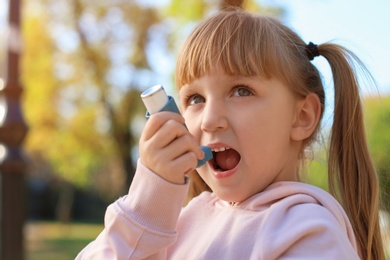 Little girl using asthma inhaler outdoors. Health care