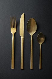 Photo of Elegant golden cutlery on black background, flat lay