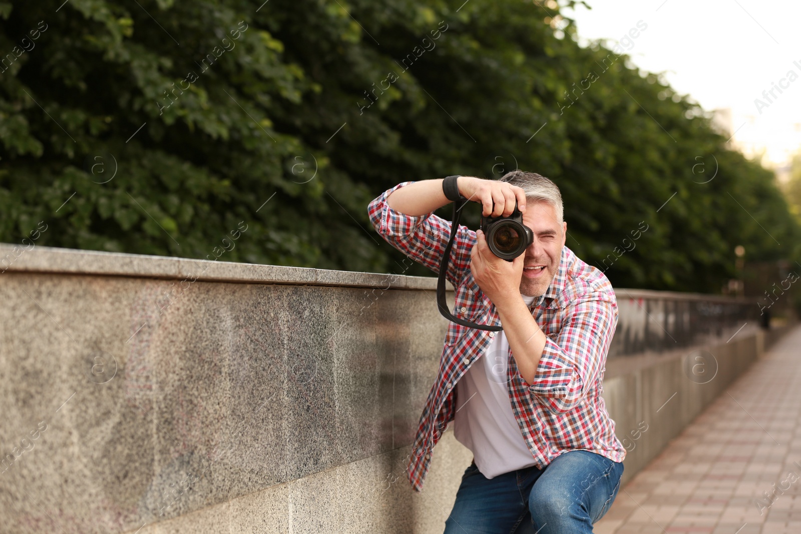 Photo of Handsome mature man taking photo with professional camera outdoors. Space for text