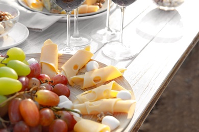 Red wine and snacks served for picnic on white wooden table outdoors