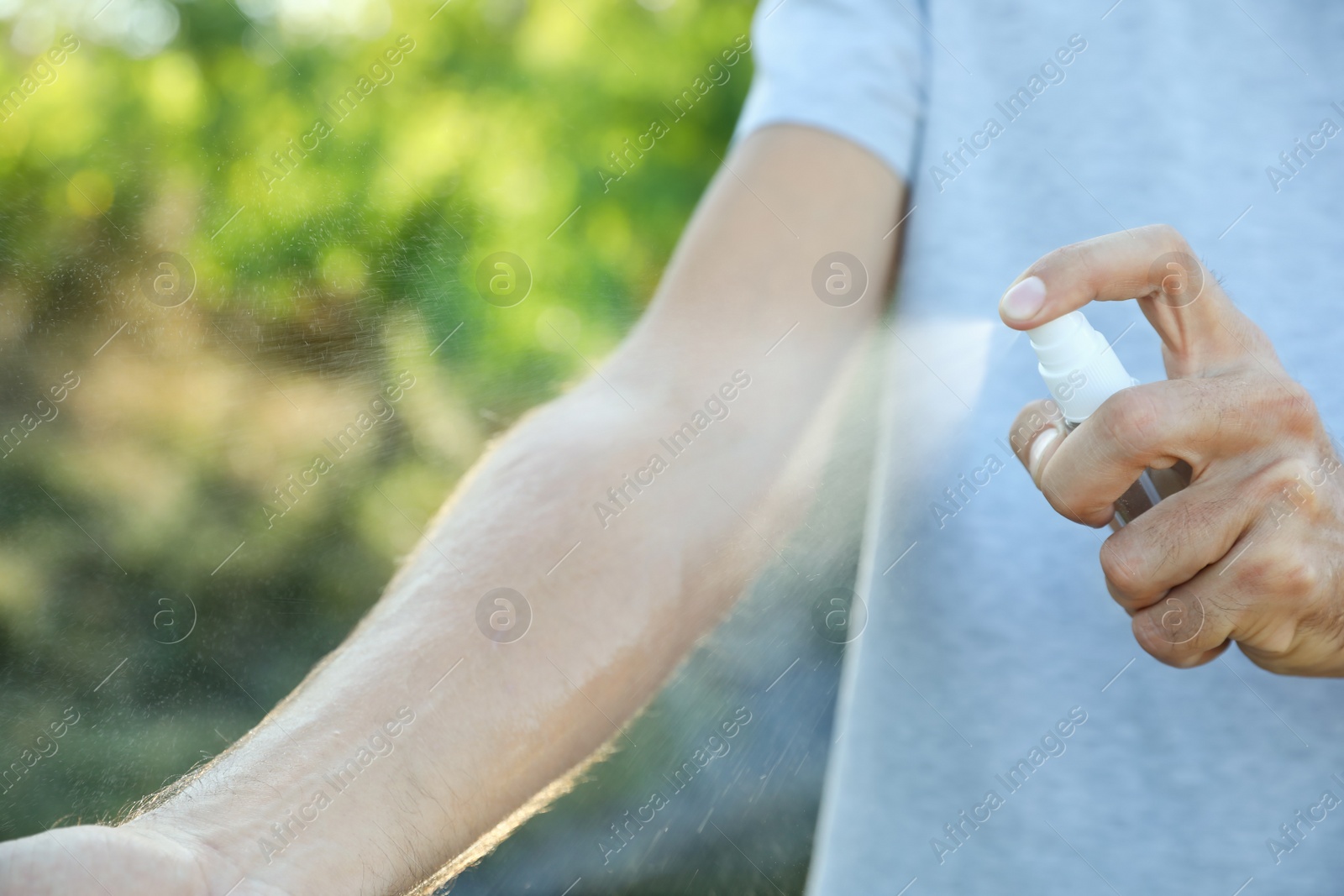 Photo of Man applying insect repellent onto arm outdoors, closeup