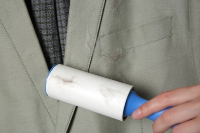 Photo of Woman removing hair from light grey jacket with lint roller, closeup