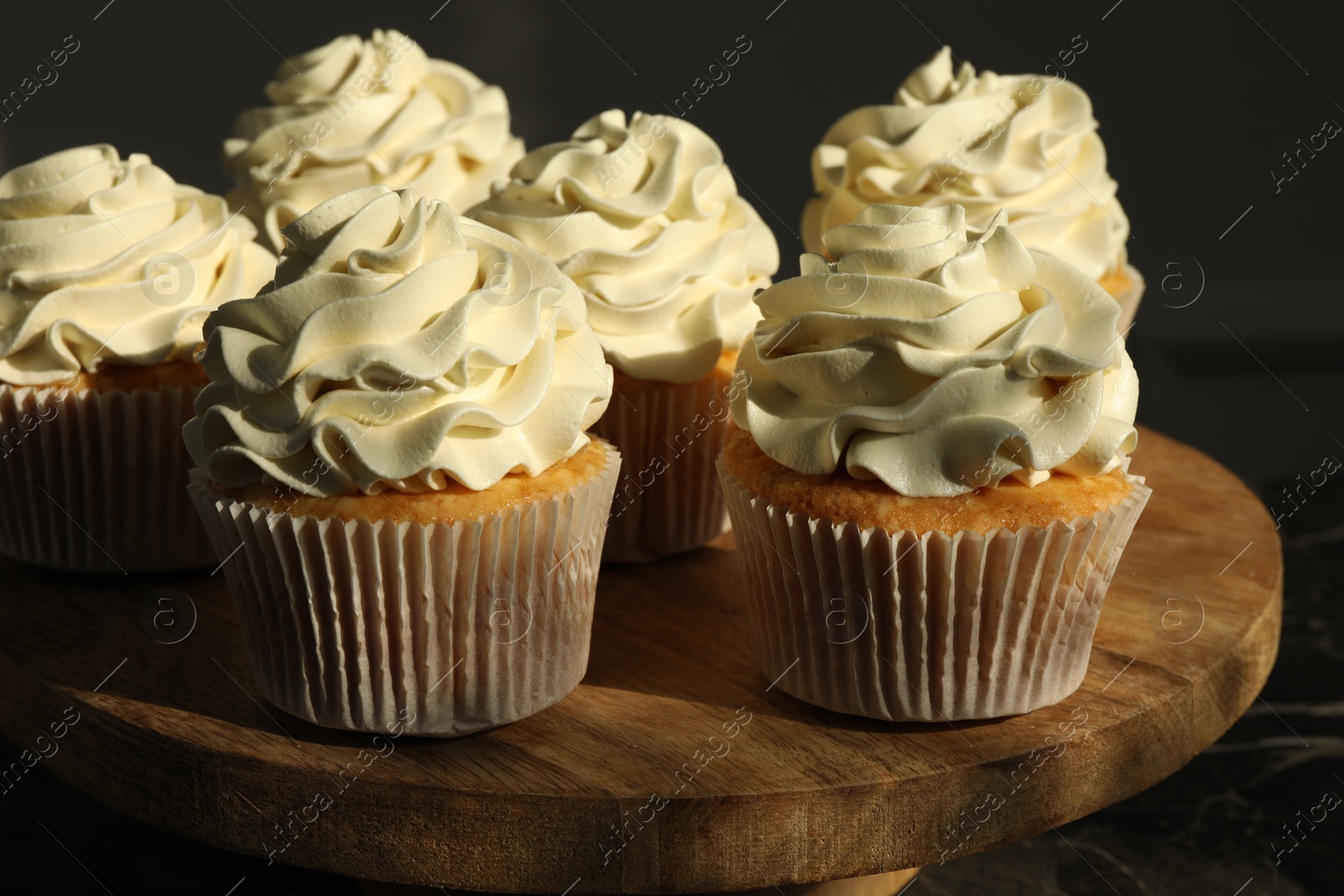 Photo of Tasty cupcakes with vanilla cream on wooden stand, closeup