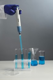 Laboratory analysis. Scientist dripping sample with micropipette into test tube at white wooden table, closeup