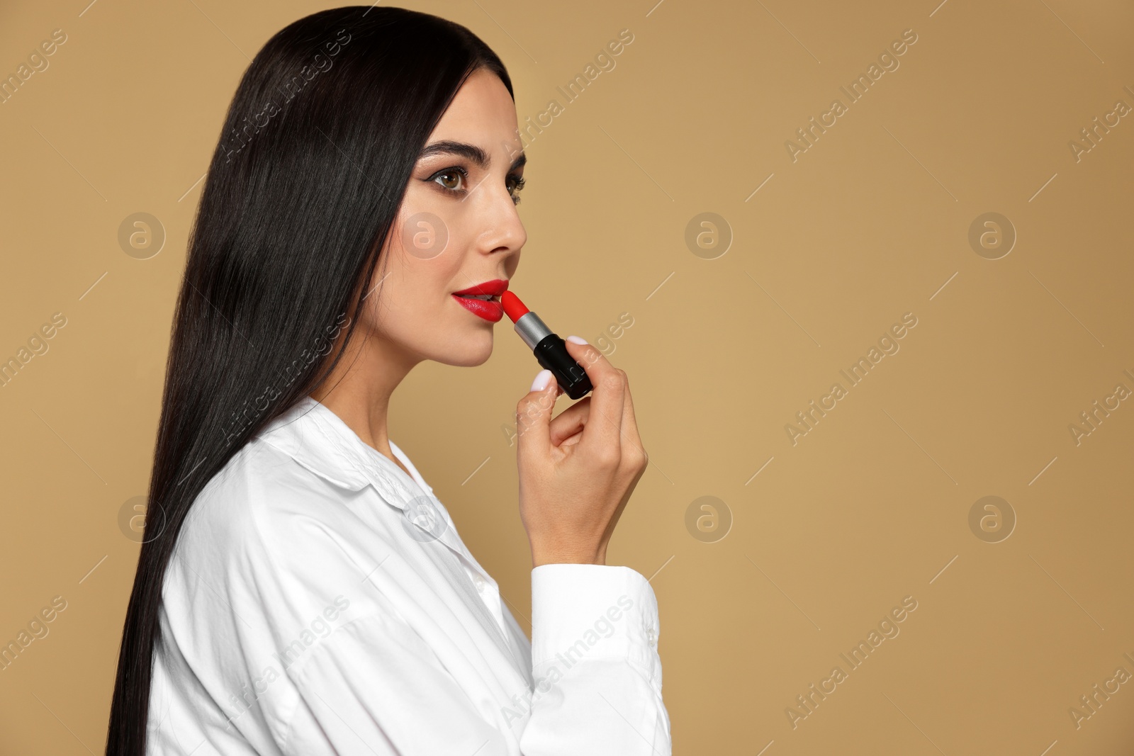 Photo of Beautiful young woman applying red lipstick on beige background, space for text