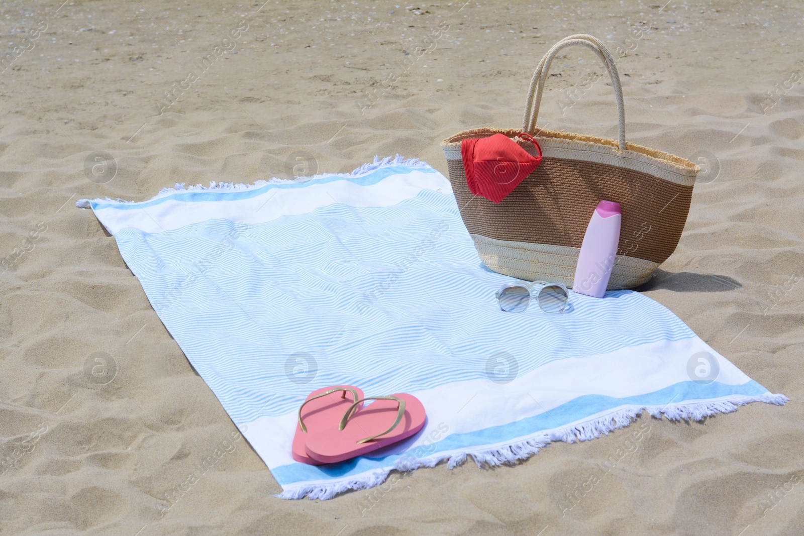 Photo of Light blue striped towel with bag, flip flops, sunglasses and sunblock on sandy beach