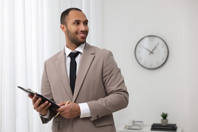 Photo of Portrait of smiling young man with clipboard and pen in office, space for text. Lawyer, businessman, accountant or manager