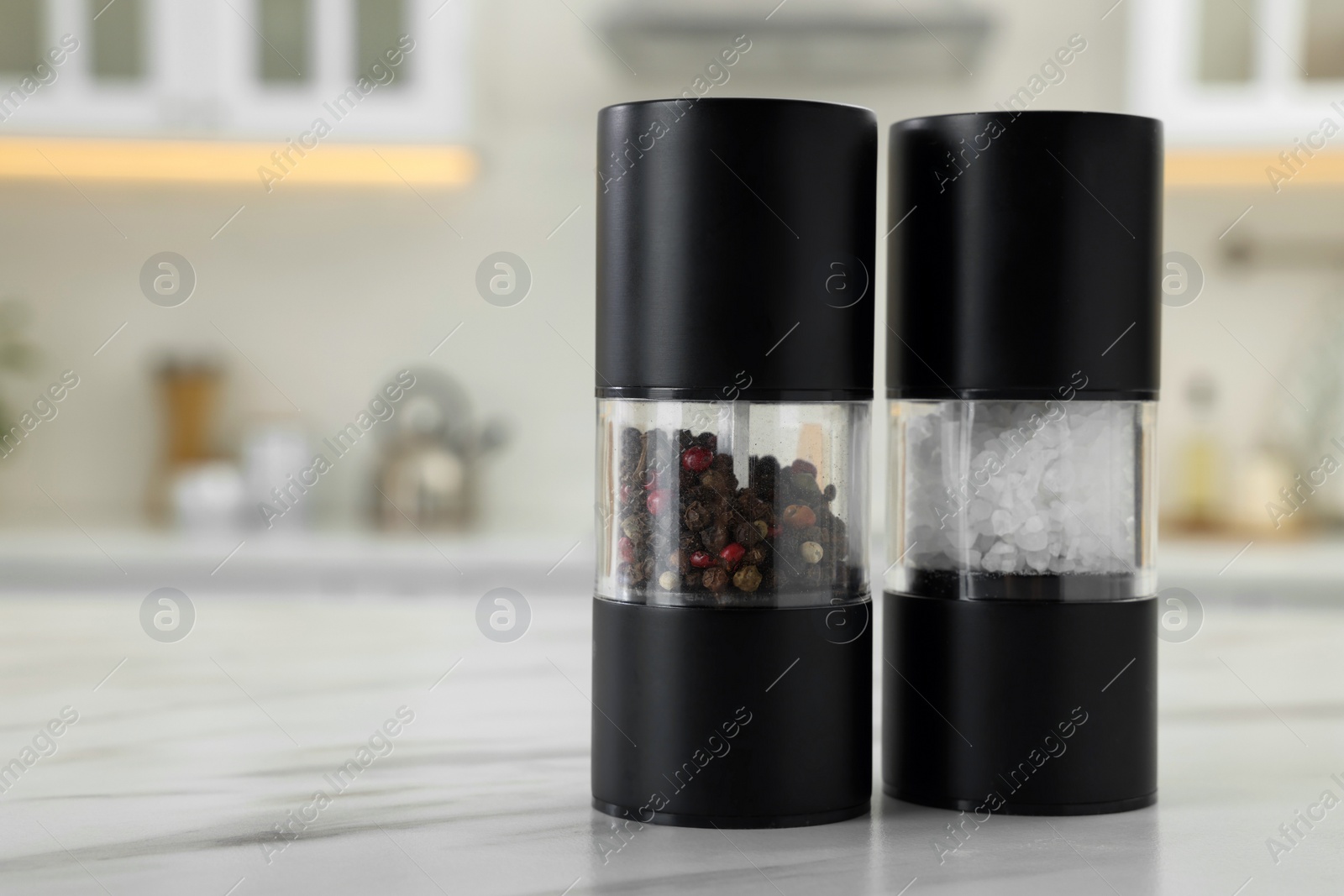 Photo of Salt and pepper mills on white marble table in kitchen. Space for text