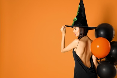 Photo of Beautiful woman wearing witch costume with balloons for Halloween party on yellow background, space for text