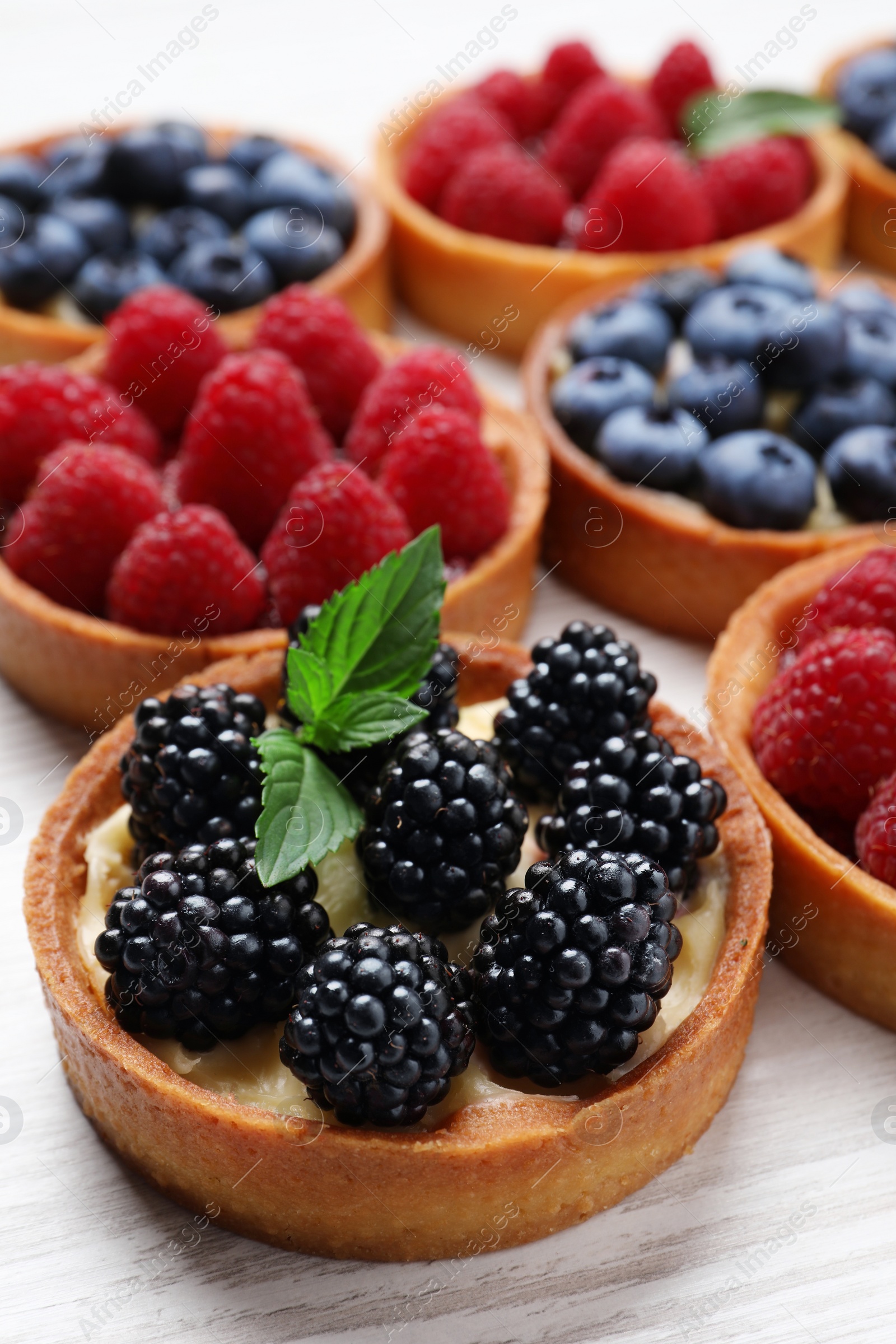 Photo of Tartlets with different fresh berries on white wooden table, closeup. Delicious dessert