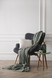 Modern armchair with knitted blanket and cushion in stylish room interior